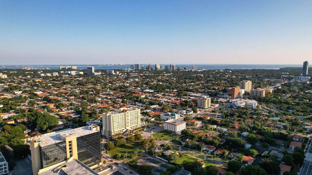 Aerial view over a Florida coastal community at golden hour, showing single-family neighborhoods running toward the Miami skyline