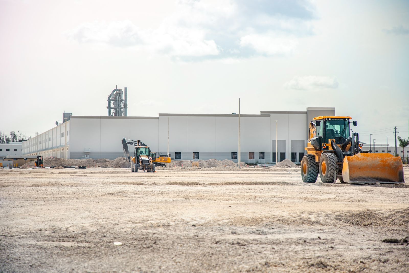 Heavy earthmoving equipment on a Florida commercial construction site with a completed warehouse in the background