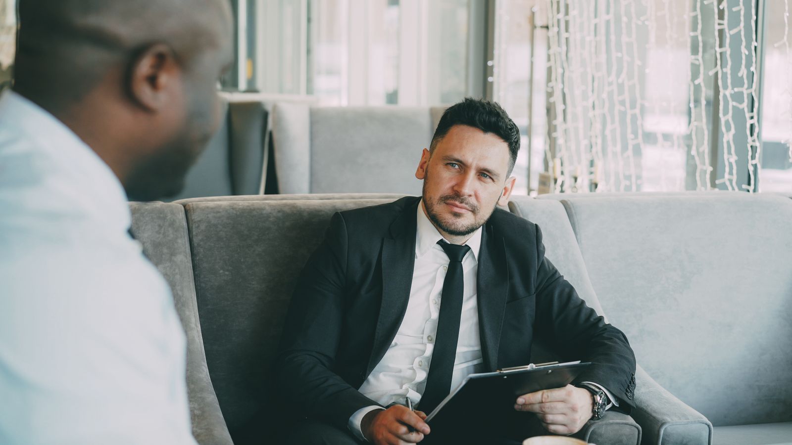 Two professionals in a private lounge discussing investment structure over a clipboard